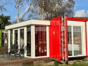 a red and white house with a chair on a deck at Containerwoning op schitterende locatie in Milsbeek