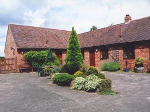 a brick building with bushes and trees in front of it at Stildon Manor Cottage in Pensax