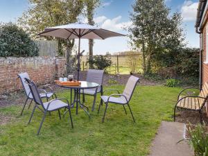 una mesa y sillas con una sombrilla en un patio en Rosemary Cottage en Stalham