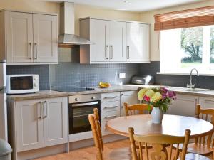 una cocina con armarios blancos y una mesa con flores. en The Granary Cottage, en Warenford