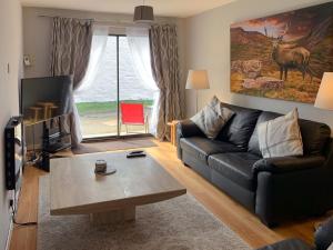 ein Wohnzimmer mit einem schwarzen Sofa und einem Tisch in der Unterkunft Crossburn Hideaway in Helensburgh