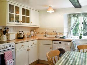 cocina con armarios blancos y lavavajillas en Yew Tree Cottage en Arford