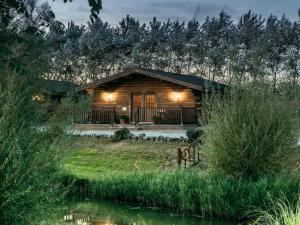 Cabaña de madera con luces frente a un estanque en Lake View Lodges - 25074, en Leake Common Side