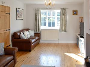 a living room with a leather couch and a window at Woodbrook Cottage in Bridport