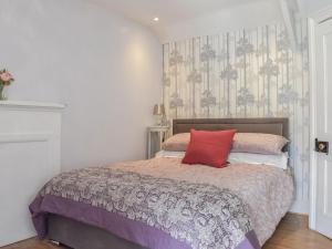 a bedroom with a bed with a red pillow on it at Keepershield Cottage in Gunnerton