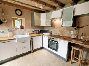 una cocina con armarios blancos y un reloj en la pared en Cornstore Cottage en Highpeak Junction