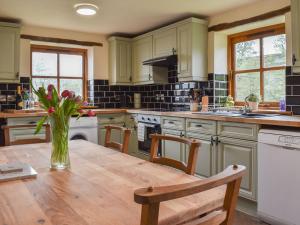 a kitchen with a wooden table with a vase of flowers at Beck Foot Cottage in Sedbergh