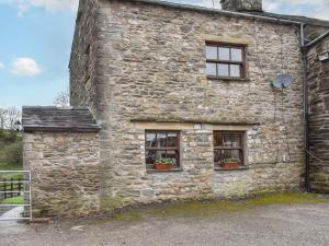 an old stone building with two windows and potted plants at Beck Foot Cottage in Sedbergh