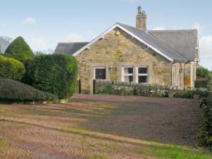 a stone house with a fence and a yard at Heckley Cottage in Alnwick