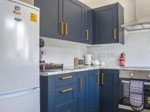 a kitchen with blue cabinets and a white refrigerator at Seashell House in Burnham on Sea