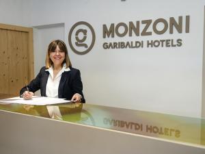 Una donna in piedi dietro un bancone davanti a un cartello di GH Hotel Monzoni a Pozza di Fassa