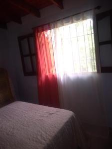 1 dormitorio con 1 cama con cortina roja y ventana en Cabaña en las sierras de Cosquín PB en Cosquín