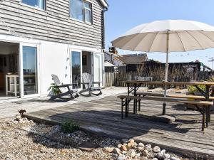 eine Holzterrasse mit einem Tisch und einem Sonnenschirm in der Unterkunft Gull House in Dungeness