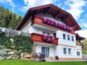 Cette maison blanche dispose d'un balcon orné de fleurs violettes. dans l'établissement Ferienwohnung Michaela, à Flattach