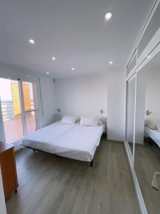 een witte slaapkamer met een bed en een groot raam bij Ático con terraza a 100 metros de la playa - Port Aventura in La Pineda