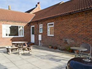 un patio con due tavoli da picnic e un edificio in mattoni di Ivy Grange Cottage a Wistow