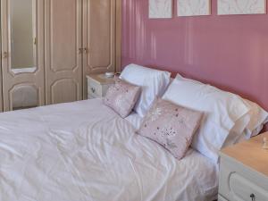 ein Bett mit weißer Bettwäsche und rosa Kissen darauf in der Unterkunft Squires Bungalow in Gunton