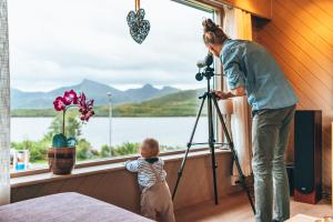 Una mujer con una cámara y un niño mirando por la ventana en Midt i Lofoten, en Alstad