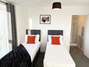 two beds in a room with white and orange pillows at Riverside Apartment Chelmsford in Chelmsford