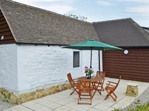 a patio with a table and chairs and an umbrella at Cornbrash Farm Cottage in Dallington