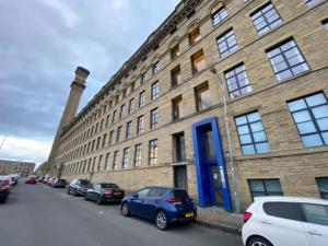 een groot bakstenen gebouw met auto's geparkeerd voor het bij Lister Mills, Apartment 327, Silk Warehouse, Lilycroft Rd, BD9 5BD in Bradford