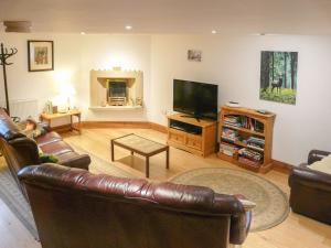 a living room with a leather couch and a television at Hollin Bank Cottage in Salterforth