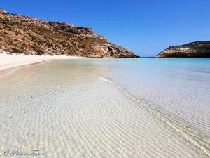 een strand met zand en water en een berg bij Élite Lampedusa in Lampedusa