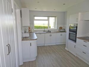 a white kitchen with white cabinets and a window at Tregoona in Crantock