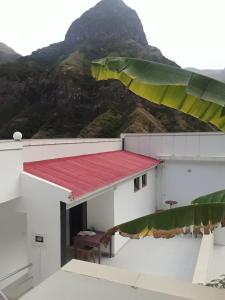 a building with a red roof with a mountain in the background at CASA MINGA & TATOL in Ribeira Grande