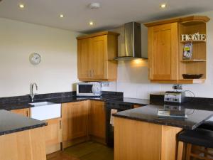 Durham Cottage-27765 في Wolsingham: مطبخ مع خزائن خشبية وقمم منضدة سوداء
