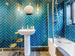 a bathroom with blue tiled walls and a sink and a tub at The Telephone Exchange in Codford Saint Mary