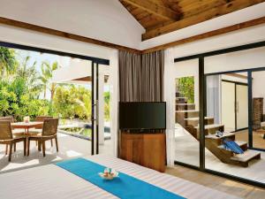 a bedroom with a large bed with a television and a table at Mӧvenpick Resort Kuredhivaru Maldives in Manadhoo