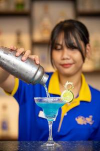 Uma mulher a derramar uma bebida azul num copo de martini. em Nangkol Village em Phnom Penh