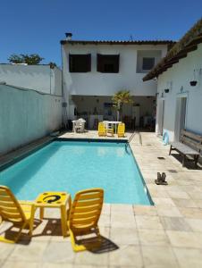 uma piscina com duas cadeiras amarelas e uma casa em Pousada Sol da Manhã no Guarujá