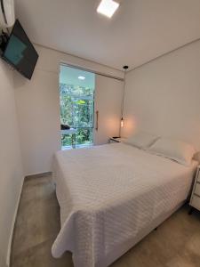 1 dormitorio con cama blanca y ventana en Maresias Beach Housing - Mata Azul, en São Sebastião
