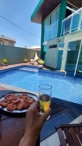 una persona sosteniendo un vaso de cerveza junto a un plato de comida en Casa de luxo em condomínio, en Arraial do Cabo