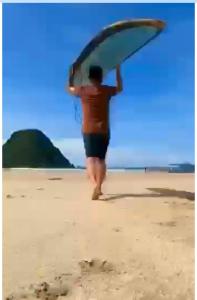 Ein Mann läuft am Strand mit einem Surfbrett auf dem Kopf in der Unterkunft Red island villas in Banyuwangi