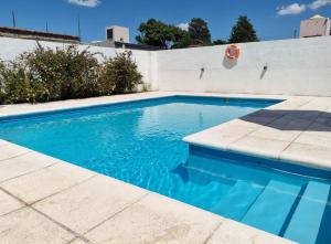 uma piscina com água azul em frente a uma parede branca em Posada de Los Lirios em Villa Carlos Paz