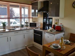 a kitchen with white cabinets and a wooden table at Puffin Cottage in Wroxham