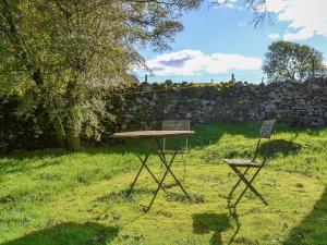 uma mesa e duas cadeiras num quintal com uma parede de pedra em Birkerthwaite Barn-w41478 em Eskdale