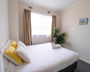 a bedroom with a bed with yellow pillows and a window at Mermaid Apartments in Merimbula