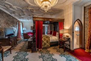 a bedroom with a bed with red curtains and a chandelier at Thornbury Castle - A Relais & Chateaux Hotel in Thornbury