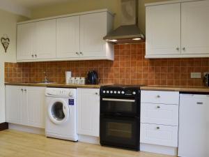 cocina con armarios blancos y lavadora en Barnex en Clippesby