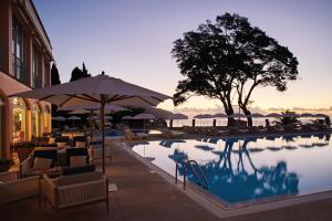 uma piscina com cadeiras e um guarda-sol junto à água em Reid's Palace, A Belmond Hotel, Madeira em Funchal