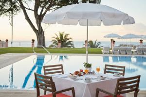 - une table à manger avec un parasol blanc à côté de la piscine dans l'établissement Reid's Palace, A Belmond Hotel, Madeira, à Funchal