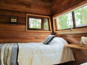 a bed in a log cabin with two windows at Los Lingues Lodge in Puerto Octay