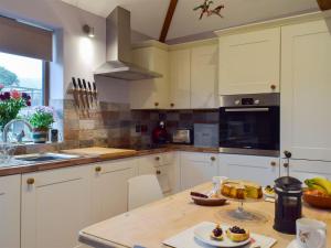 a kitchen with white cabinets and a wooden table at Chick Hatch Barn in Kelsale