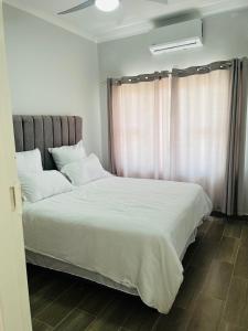 a bedroom with a bed with white sheets and a window at Zanaya Apartments in Gaborone