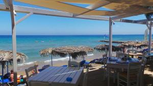 a beach with tables and straw umbrellas and the ocean at Fiore Beach Studios in Vasilikos