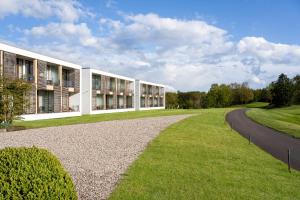 a building with a road next to a grass field at Angel's - das hotel am golfpark in Sankt Wendel